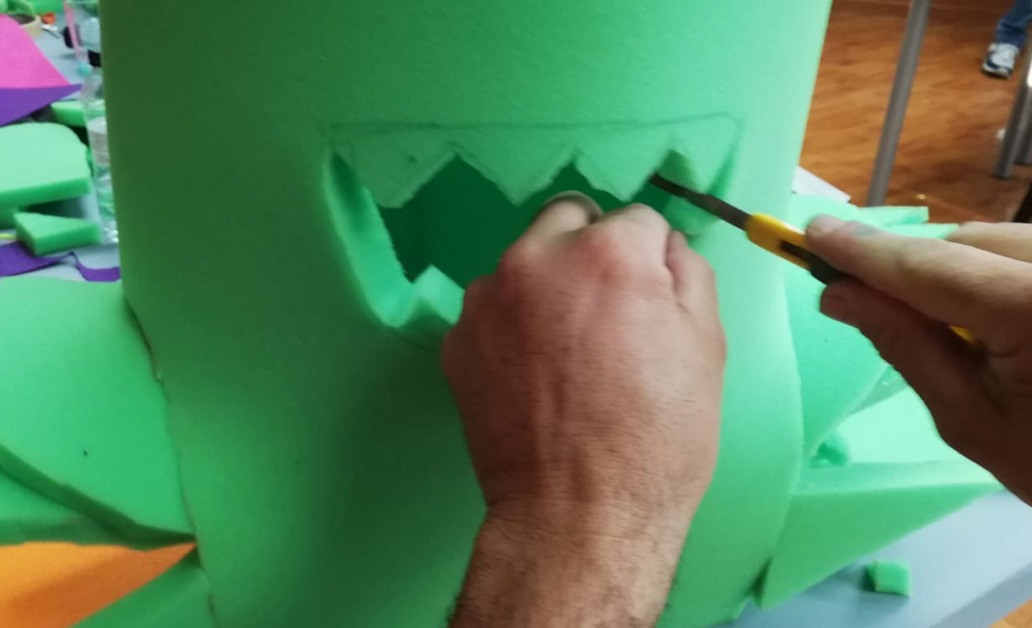 Recortando con cúter la boca dentada en un cilindro de espuma verde para el disfraz