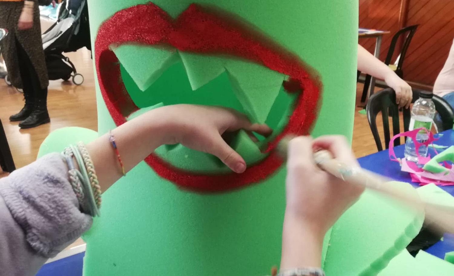Pintando de rojo el contorno de la boca dentada del disfraz de espuma