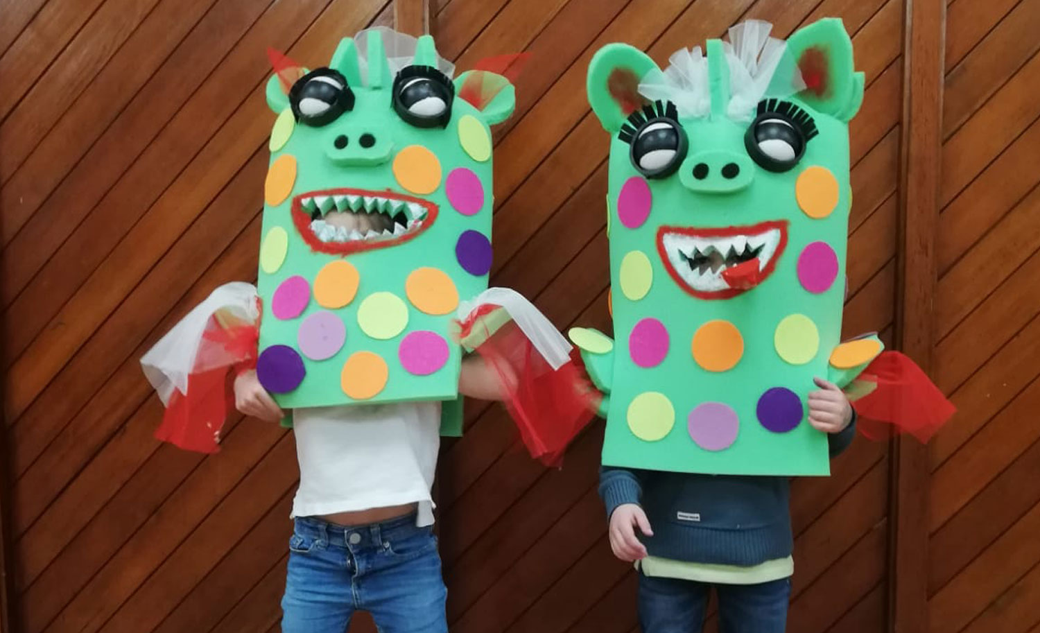 Disfraces con espuma de colores terminados, puestos por dos niños que agitan sus alas de tul rojo.